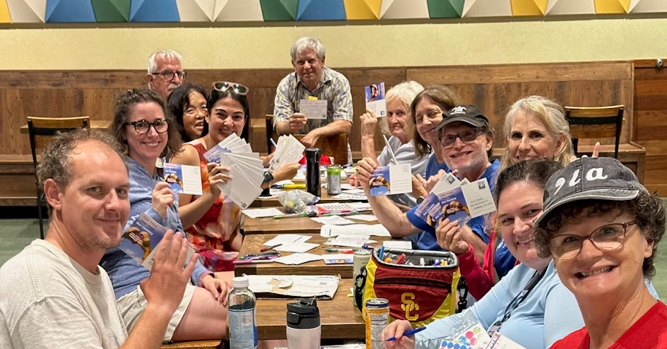 Group of people posing with their postcards at the weekly postcarding party in Kailua, hosted by the Blue Wave and Indivisible Windward Oahu.